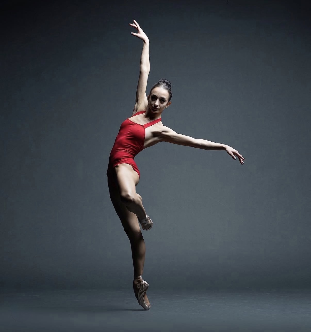 Buse Babadag in red leotard, en pointe on gray backdrop