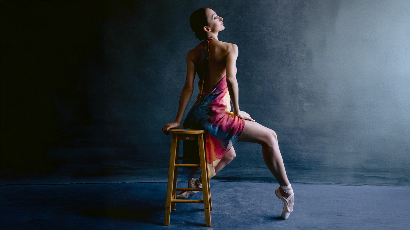 Buse Babadag seated on stool in colorful dress en pointe — studio portrait